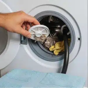 A close-up of a person's hand pulling a dirty filter from the front of a washing machine.